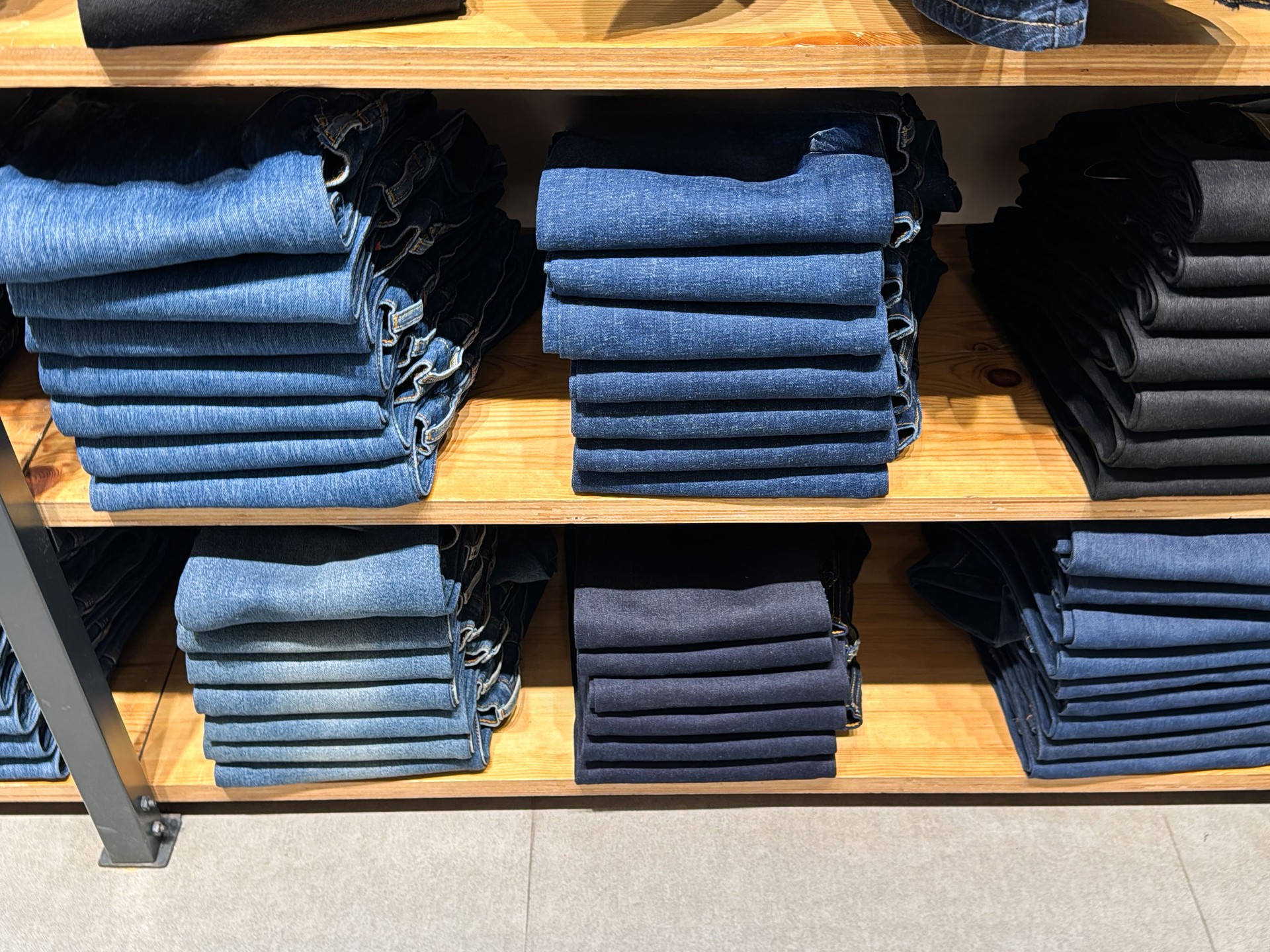 Image of piles of folded, black, stone washed, bleached and blue denim jeans on clothing department store display shelves, casual clothing, elevated view, focus on foreground